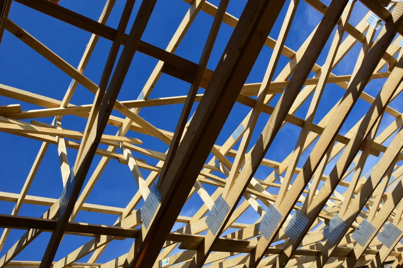 Looking up through new roof trusses at a clear blue sky.