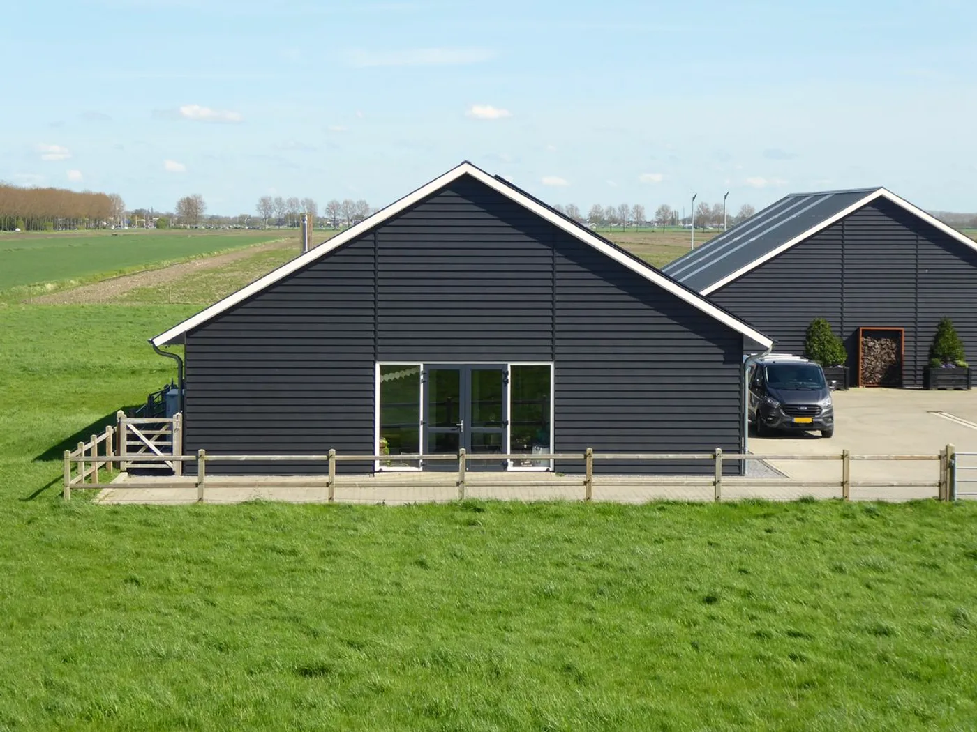 A finished home with black board cladding and a gabled roof, on flat green farmland.
