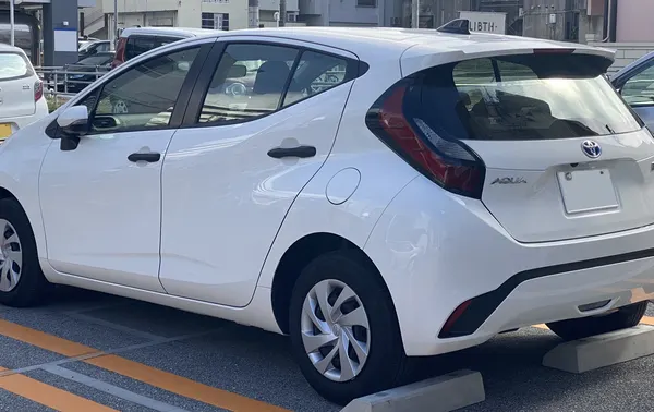 A white Toyota Aqua hatchback seen from the rear quarter in a parking space.