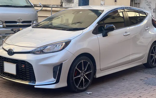 A white Toyota Aqua GR Sport hatchback with black alloy wheels parked on a paved street.
