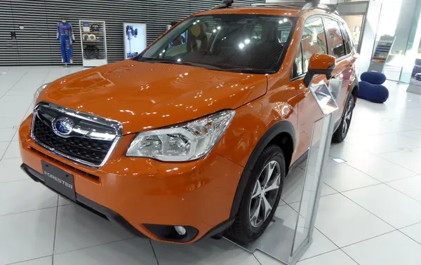 An orange Subaru Forester SUV with roof rails on a pale tiled floor.