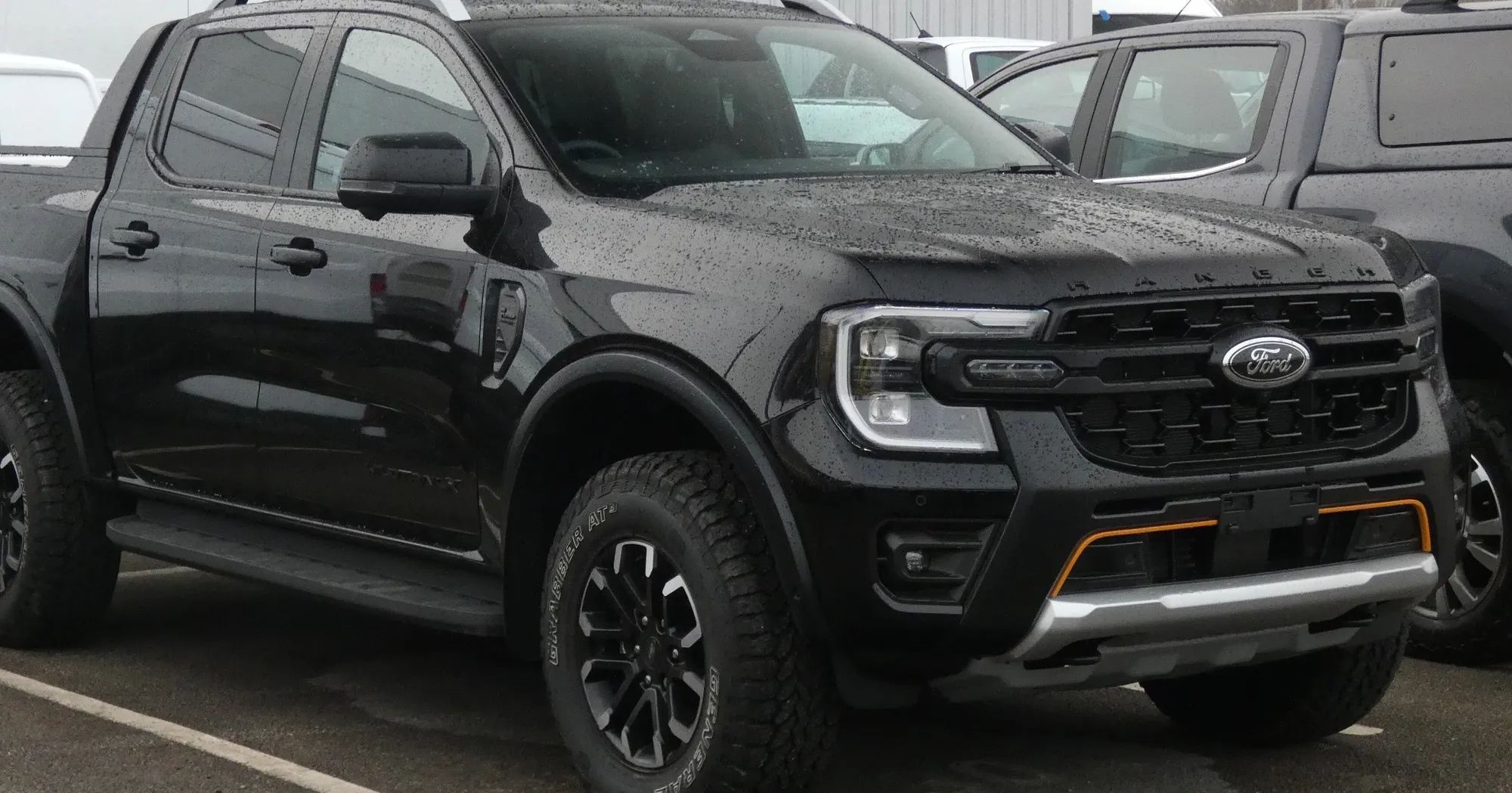 A black Ford Ranger double cab ute parked on a wet yard under a grey sky.