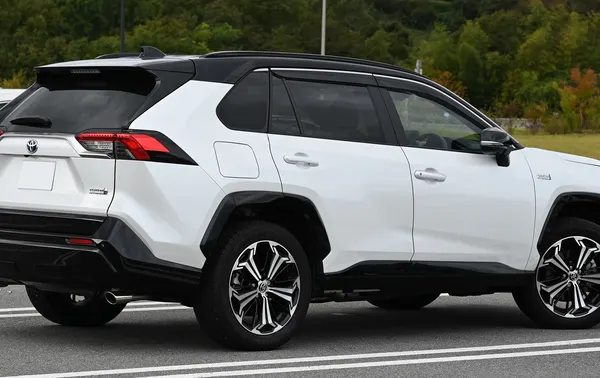 A white Toyota RAV4 with a black roof seen from the rear quarter beside a line of trees.