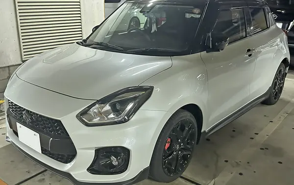 A white Suzuki Swift Sport with a black roof and red brake callipers in a parking garage.