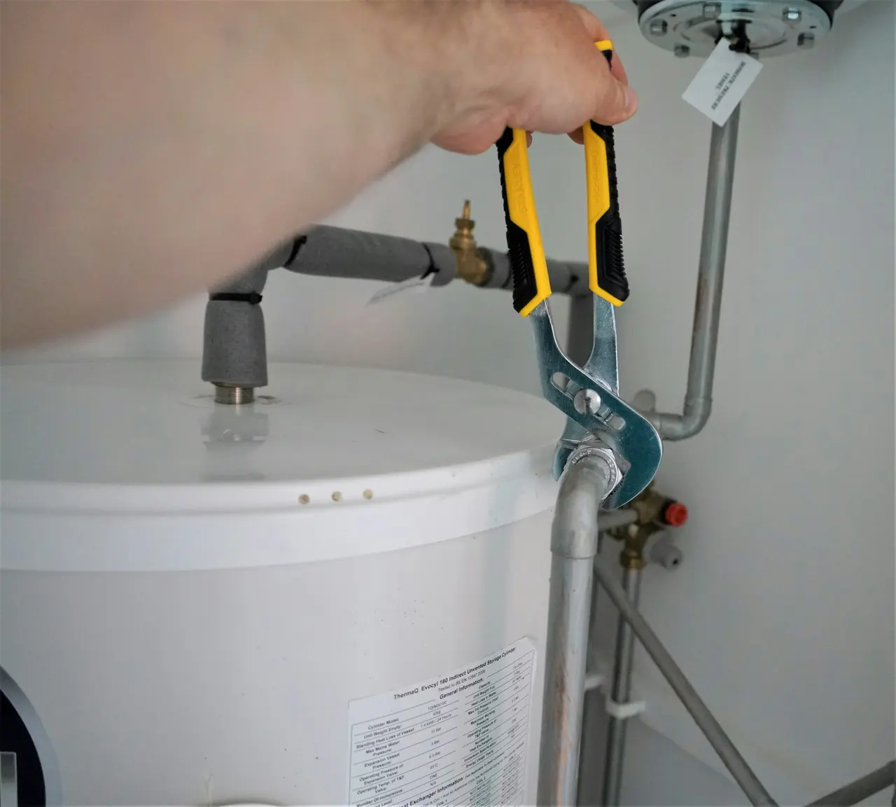 A wrench tightening a fitting on top of a hot water cylinder